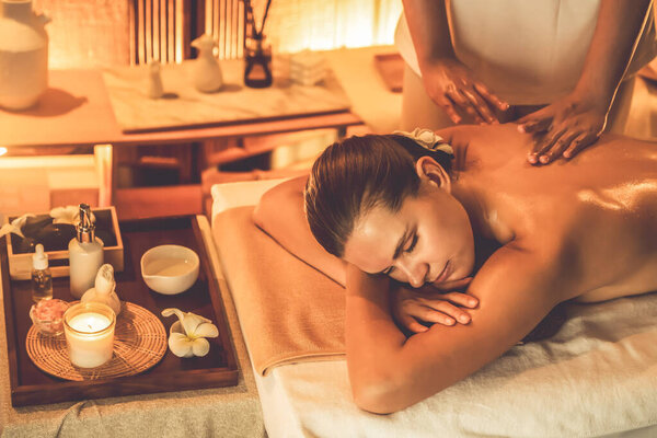Caucasian woman customer enjoying relaxing anti-stress spa massage and pampering with beauty skin recreation leisure in warm candle lighting ambient salon spa at luxury resort or hotel. Quiescent