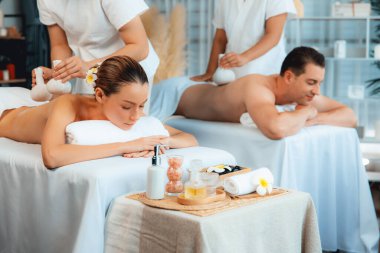 Sıcak bitkisel top spa masaj vücut tedavisi, masör nazikçe bitki torbasını çift müşteri vücuduna bastırıyor. Aromaterapi dinlenme sükuneti ve sükuneti kaplıca salonundaki atmosferi aydınlatıyor. Sessiz.