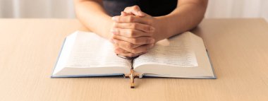 Ahşap masada kutsal İncil 'in üzerinde haç tutan dua eden erkek eli görüntüsü. Üst Manzara. Umut, din, inanç, Hıristiyanlık ve Tanrı 'nın kutsaması kavramı. Sıcak ve kahverengi arka plan gelişiyor..