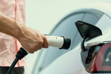 Dışarıdaki şarj istasyonundan EV şarj aletini şarj etmek için elektrikli araca elle tak. Alternatif temiz ve sürdürülebilir enerji kavramına sahip taze gün ışığı ortamı. Kalıcı