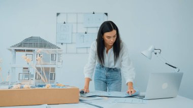 Genç, güzel beyaz bir mimar masanın üzerine plan koyar ve ev modeliyle karşılaştırırken, modern ofisteki fahişe modellerini dikkatlice incelerken arkadaki çizgilerle karşılaştırır. Tertemiz..
