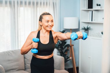 Atletik ve sportif yaşlı bir kadın, emekli olduktan sonra vücut ağırlığına uygun sağlıklı vücut konsepti olarak evde dambıl kaldırarak vücut egzersizi yapıyor. Etki