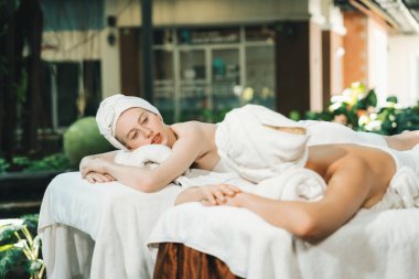 Beyaz havluyla beyaz bir spa yatağında dinlenen ve profesyonel bir masaj salonundaki masörle vücut masajı yapan birkaç güzel beyaz kadının portresi. Huzur..