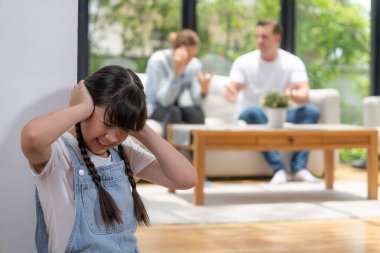 Stresli ve mutsuz kız köşede toplanır, ailesi arka planda tartışırken kulaklarını acılı bir ifadeyle kapatır. Aile içi şiddet ve travmatik çocukluk depresyona dönüşür. Eşzamanlama