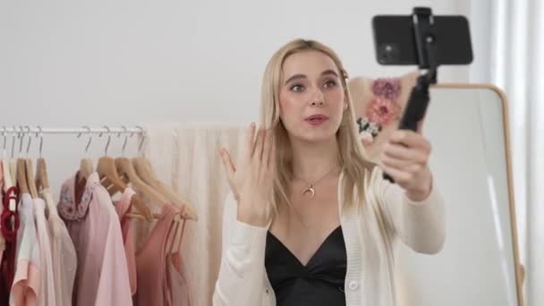 若いソーシャルメディアコンテンツクリエイターの女性は セルフィースティックを使用してファッションビデオを作ります 説得力のあるオンライン衣料品を作っている間 ブロガーはカメラに微笑み 視聴者やフォロワーにブロガーを販売します ブリテット — ストック動画