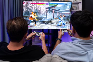 Oyun arkadaşları savaş sanatları dövüşçülerinin video oyununu arka plandaki joystickleri kullanarak oynuyorlar. Memlekette neşeli bir dövüşçüyle rahat bir neon ışığı. Satılabilir.