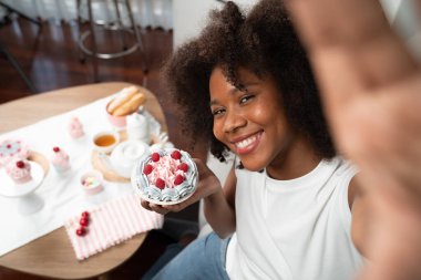 Genç ve güzel Afrikalı blogcu akıllı telefondaki selfie ile konsept özel mutfak konseptinde kek sunuyor. Favori tatlı fırın yemeğiyle sosyal medyanın yaratılması. Tatlandırıcı.