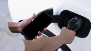 Akıllı telefon ekranı akıllı EV mobil uygulama üzerinde pil durumu EV araba garajdaki ev şarj istasyonu ile elektrik şarj ederken. Geleceğin yenilikçi EV arabası ve enerji sürdürülebilirliği. İnceleyin