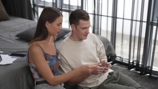 年轻夫妇坐在家里的卧室里 使用在线支付应用程序和智能手机上的数字钱包来支付信用卡 电子商务购物和通过移动互联网进行现代采购 — 图库视频影像
