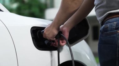 Adam evdeki şarj istasyonundan elektrikli arabasını EV şarj cihazıyla şarj ediyor. EV arabaların teknolojik gelişimi ve gelecekteki sürdürülebilir enerji için ev enerjisi altyapısı. İnceleyin