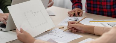 Erkek mühendis mimarlık bürosunda dizüstü bilgisayar üzerinde çalışırken, yetenekli mimar kağıt üzerinde taslak hazırlıyor. Profesyonel mühendis ve mimar mimari projede işbirliği yaparlar. - Yakın çekim. Tanımlama.