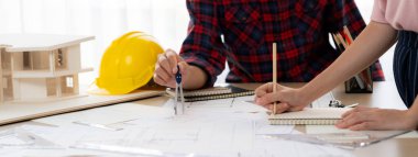 Kooperatif mimar ekibinin kesilmiş görüntüsü ev modeli, güvenlik miğferi ve mimari planlarla toplantı masasında birlikte çalışmaya karar verir ve birlikte çalışırlar. - Yakın çekim. Eline odaklan. Filizlenen.