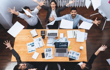 Üst düzey ofis çalışanı toplantı odasında kutlama yapıyor, evrak işlerini havaya fırlatıyor. İş adamlarından gelen heyecan ve özgürlük ifadesi, finansal analiz kağıtlarını kutlama jesti olarak fırlatıyor. Uyum