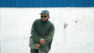 Sokak ortasında mavi duvarlı hippi dansçı ayak basamağı. Asyalı break dansçı kollarını açarken sokak dansı yapıyor. Hip hop koreografı enerjik bir dans sergiliyor. Açık hava sporu 2024. ÇalışmaComment.