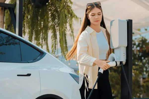 若い女性は緑の市立公園の駐車場でEv電気自動車を再充電する バッテリー充電ステーションを備えた環境に優しいEvカーのための都市持続可能性ライフスタイル エクスペディエント — ストック写真