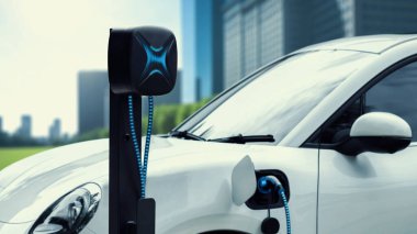 EV şarj kablosu ile elektrik yüklemek için elektrik istasyonuna eko yeşil şehir parkındaki elektrik kablosu takıldı. Geleceğin yenilikçi EV arabası alternatif temiz enerji kullanarak CO2 'yi azaltıyor. İnceleyin
