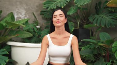 Sabah yoga ve meditasyon yapan genç bir kadın bitki yaprağıyla doğal bahçede yalnızlığın tadını çıkarıyor ve meditasyon yapıyor. Farkındalık aktivitesi ve sağlıklı zihin yaşam tarzı. Blithe