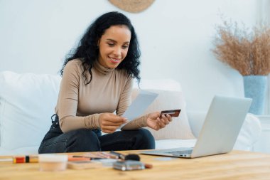 Genç mutlu bir kadın internetten alışveriş yaparak ürün satın alırken aynı zamanda internet üzerinden online kredi kartı ödeme sistemi ile çevrimiçi mağaza platformundan önemli siber güvenlik tarafından korunan ürünler sipariş ediyor.