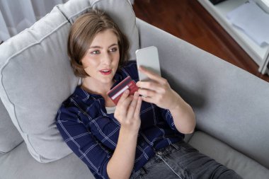 Genç mutlu kadın internetten alışveriş yaparak ürün satın alırken aynı zamanda internet üzerinden online ödeme sistemi ile çevrimiçi mağaza platformundan en yüksek siber güvenlik tarafından korunan ürünler sipariş ediyor.