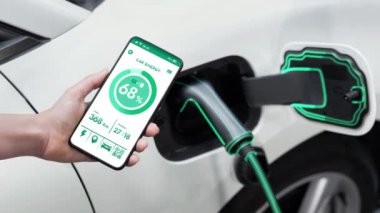 Akıllı telefon akü durumu arayüzünü elinde tutan iş kadını akıllı EV mobil uygulama ile otomobil parkındaki şarj istasyonundan elektrik şarj eden çevre dostu EV araba. İnceleyin
