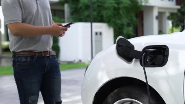 現代のライフスタイルの男は家庭の充電ステーションで電気自動車にEv充電器を挿入し スマートフォンでEvバッテリーの状態を有効にしました 未来的なエネルギーの持続可能性と電気自動車 パーセント — ストック動画