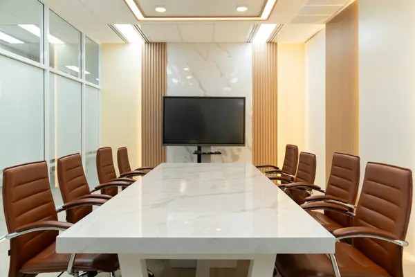 Modern meeting room interior with television for remote working. Modern white meeting table with chairs. Conference room surrounded by glass wall. No people. TV screen office background. Ornamented.