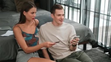 Genç çift, kredi kartıyla ödemek için internet üzerinden ödeme uygulaması ve dijital cüzdan kullanarak yatak odasında oturuyor. Mobil internet üzerinden alışveriş ve modern alımlar. Düzenle
