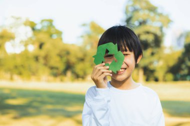 Cheerful young asian boy holding recycle symbol on daylight natural green park promoting waste recycle, reduce, and reuse encouragement for eco sustainable awareness for future generation. Gyre clipart