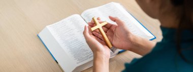 Dişi Tanrı inananı, açık ahşap kilise masasında kutsal kitap üzerinde ahşap haç tutuyor. Üst Manzara. Umut, din, inanç, Hıristiyanlık ve Tanrı 'nın kutsaması kavramı. Sıcak bir arka plan. Filizlenen.