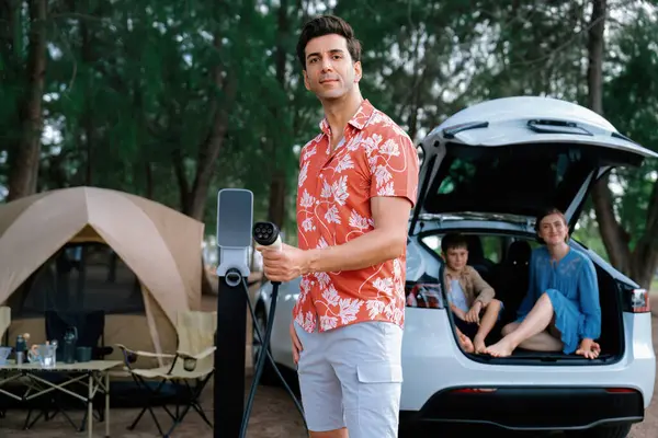 stock image Outdoor adventure and family vacation camping in nature travel by eco friendly car for sustainable future. Lovely family recharge EV car with EV charging station in campsite. Perpetual