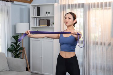 Enerjik kadın evde egzersiz yapıyor, kas kazanmak için direnç bandını esnetiyor. Genç atletik Asyalı kadın dayanıklılığı ve dayanıklılık antrenmanı ev ödevi rutin konsepti olarak..