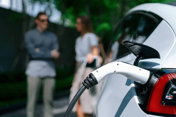 夏季乘坐电动车在绿色可持续城市室外花园充电的年轻夫妇通过电动车内部的绿色清洁充电能源展示了城市可持续发展的生活方式 — 图库照片