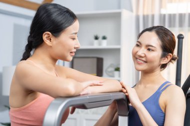 Enerjik ve güçlü atletik Asyalı kadın evde spor arkadaşı ya da antrenörü ile birlikte eliptik koşu makinesiyle koşuyor. Formda fiziğin takibi ve sağlıklı yaşam tarzına bağlılık. Kuvvetli