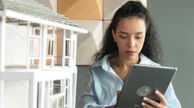 Genç, güzel İspanyol mimar mühendis modern ofisteki ev modeli yapısını kontrol ederken tablet kullanarak bina inşaatını çiziyor. Yaratıcı iş inşaat konsepti. Yönlendirici.