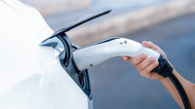 Çocuklar elektrikli araca EV şarj prizi takıp açık hava şarj istasyonundan EV araba aküsünü şarj ediyorlar. Alternatif temiz ve sürdürülebilir enerji kavramına sahip taze gün ışığı. Kalıcı