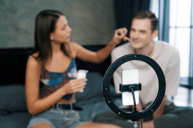 Sosyal medya için güzellik ve kozmetik video içeriği hazırlayan genç bir kadın erkek arkadaşını model ve ışık yüzüğü olarak kullanıyor. Güzellik blogcusu seyirciye ya da takipçiye güzellik bakımını gösteriyor. Açılıyor