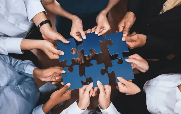 Diverse corporate officer workers collaborate in office, connecting puzzle pieces to represent partnership and teamwork. Unity and synergy in business concept by merging jigsaw puzzle. Concord