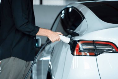 Genç adam EV elektrikli arabasıyla alışveriş merkezinin otoparkına gidiyor şehir merkezindeki şarj oluyor yeşil, temiz, yeniden şarj edilebilir elektrikli araç iç organları ile kentsel sürdürülebilirlik yaşam tarzını gösteriyor
