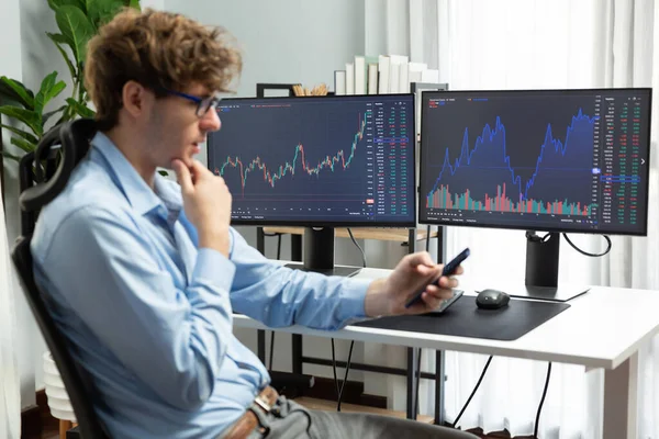 Akıllı telefona bakan genç yatırımcı, modern ofisteki mevcut piyasa grafiğinde iki dizüstü bilgisayardaki dinamik para değişimi yatırımını analiz ediyor. Toplayıcı.