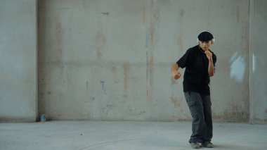 Kulaklıktan çimento arka planda müzik dinlerken break dans pratiği yapan yakışıklı bir hippi. Sokak dansçısının hareketli çekimi robot dansı yapar. Açık hava sporu 2024. Modern dans. ÇalışmaComment.