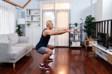 Aktif ve formda kıdemli adam oturma odasında egzersiz yapmadan önce ısınma ve esneme hareketleri yapıyor. Emeklilikten sonra sağlıklı yaşam tarzı konsepti. Etki