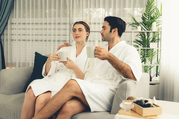 Beauty or body treatment spa salon vacation lifestyle concept with couple wearing bathrobe relaxing with drinks in luxurious hotel spa or resort room. Vacation and leisure relaxation. Quiescent