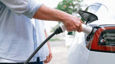 Modern çevre dostu adam EV şarj istasyonundan elektrikli aracı şarj ediyor. EV araba teknolojisi ev sakinleri için gelecekte çevresel sürdürülebilirlik için kullanılıyor. Eşzamanlama