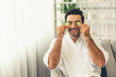 Elinde taze salatalık dilimleri tutan ve bornoz giyen bir adam tatil köyünde ya da otelde yüz bakımının keyfini çıkarıyor. Yüz ve güzellik tedavisi için cilt bakımı. Sessiz.