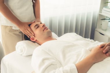 Beyaz adam stres önleyici kafa masajından ve lüks bir tatil beldesi veya otel spa salonundaki modern ışık ortamında yüz güzelliği eğlencelerini şımartmaktan hoşlanıyor. Sessiz.