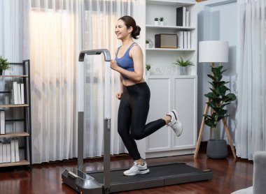 Enerjik ve güçlü atletik Asyalı kadın evde koşu makinası çalıştırıyor. Formda fiziğin takibi ve ev çalışması ve eğitimle sağlıklı yaşam tarzına bağlılık. Kuvvetli