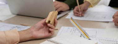 Profesyonel mimar takımı toplantı masasında mimari projeyle ilgili tartışırken planlar ve ahşap bloklar modern ofiste etrafa saçıldı. - Yakın çekim. Eline odaklan. Tanımlama.