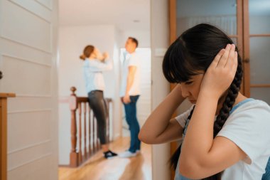 Stresli ve mutsuz genç kız köşeye kıvrılıp kulaklarını kapatarak arka planda ebeveyninin tartışmasını engelliyor. Evde aile içi şiddet ve travmatik çocukluk depresyona dönüşür. Eşzamanlama