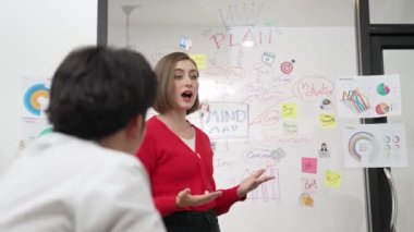 Genç ve güzel profesyonel iş kadını, yaratıcı iş toplantısında yakışıklı yönetici dinlerken zihin haritalama ve istatistiksel grafik kullanarak pazarlama fikrini kendine güvenle sunuyor. Tertemiz..