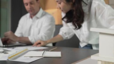 Bir grup mimar mühendis birlikte çalışıyor ve ofis tasarımı hakkında tartışıyorlar. Genç mühendis ev modelini ölçerken yönetici dizüstü bilgisayar kullanıyor. İş tasarımı konsepti. Yönlendirici.